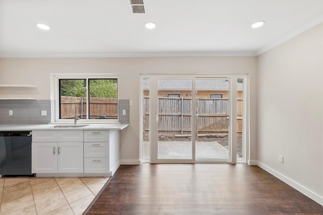 kitchen featuring white cabinets, backsplash, dishwasher, light wood-type flooring, and ornamental molding