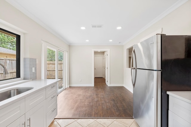 kitchen featuring stainless steel fridge, light hardwood / wood-style floors, ornamental molding, sink, and white cabinetry