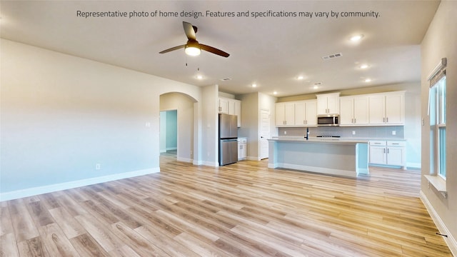 kitchen with ceiling fan, stainless steel appliances, light hardwood / wood-style floors, and an island with sink