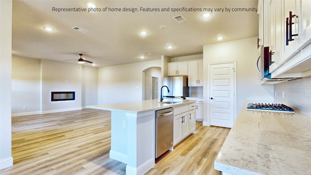 kitchen with white cabinets, stainless steel appliances, a kitchen island with sink, ceiling fan, and tasteful backsplash