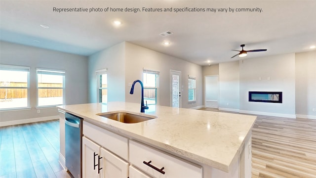 kitchen featuring light stone countertops, a center island with sink, light hardwood / wood-style flooring, sink, and ceiling fan