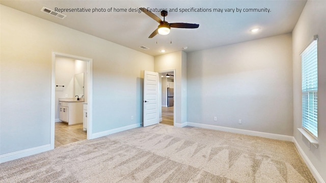 unfurnished bedroom with light colored carpet, stainless steel refrigerator, sink, ceiling fan, and connected bathroom