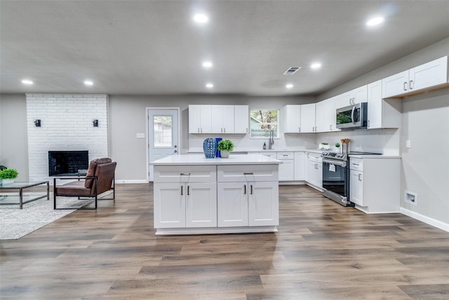 kitchen featuring dark hardwood / wood-style flooring, appliances with stainless steel finishes, white cabinetry, and a brick fireplace