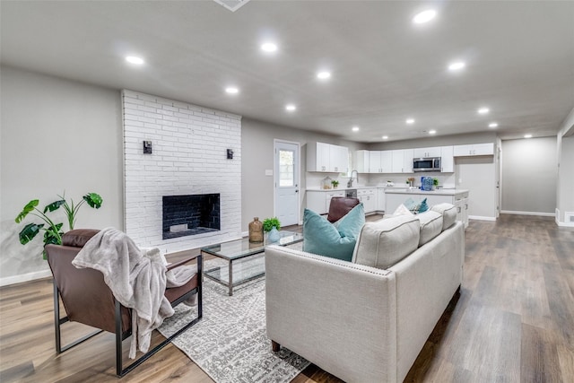 living room featuring a brick fireplace, hardwood / wood-style floors, and sink