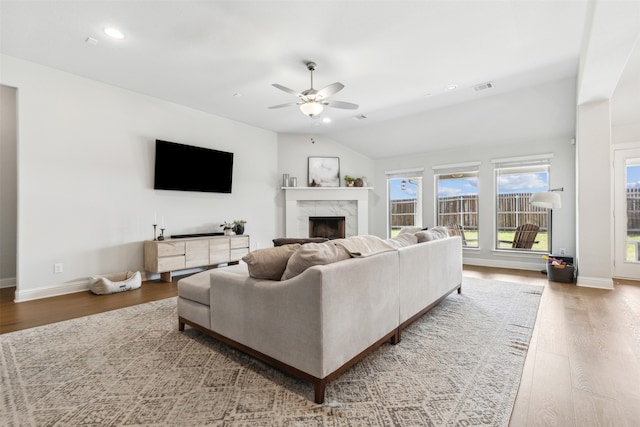 living room with hardwood / wood-style flooring, a high end fireplace, ceiling fan, and vaulted ceiling