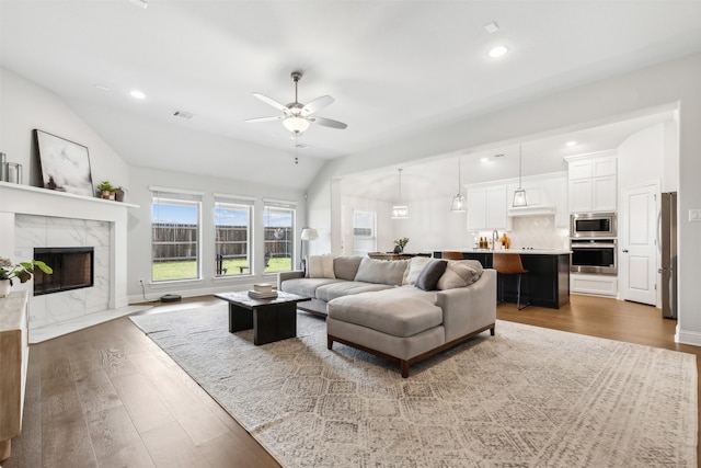 living room featuring ceiling fan, a high end fireplace, dark hardwood / wood-style floors, and vaulted ceiling