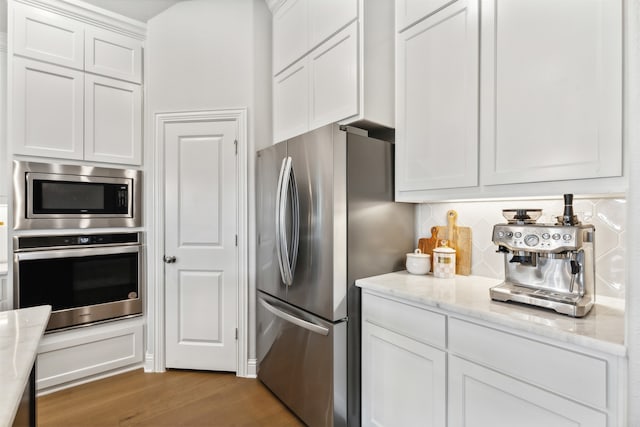 kitchen with white cabinetry, appliances with stainless steel finishes, light stone countertops, and light wood-type flooring