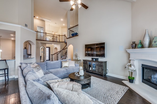 living room featuring dark wood-type flooring, ceiling fan, and a high ceiling