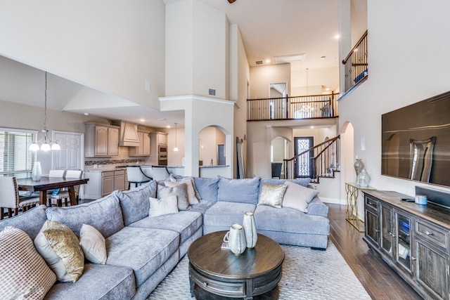 living room featuring dark wood-type flooring, a towering ceiling, and an inviting chandelier