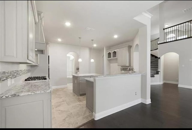 kitchen with stainless steel gas stovetop, hardwood / wood-style floors, decorative light fixtures, and kitchen peninsula