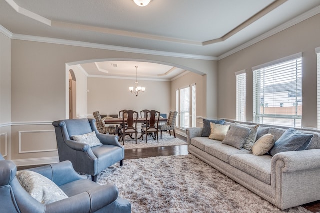 living room with wood-type flooring, a raised ceiling, a chandelier, and ornamental molding