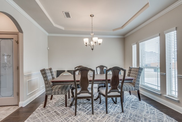 dining space with crown molding, an inviting chandelier, wood-type flooring, and a tray ceiling