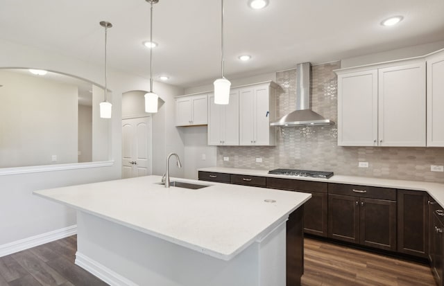 kitchen featuring sink, white cabinets, a center island with sink, decorative light fixtures, and wall chimney exhaust hood