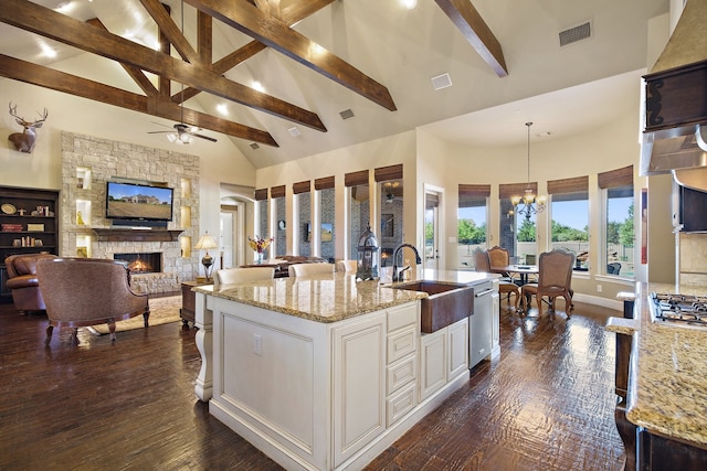 kitchen featuring hanging light fixtures, light stone countertops, high vaulted ceiling, a stone fireplace, and sink