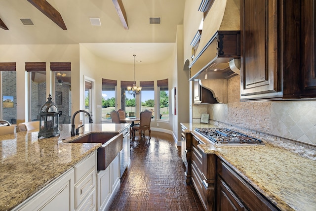 kitchen featuring sink, pendant lighting, stainless steel gas stovetop, decorative backsplash, and an inviting chandelier