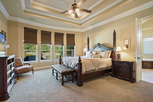 carpeted bedroom featuring ornamental molding, ensuite bath, a tray ceiling, and ceiling fan