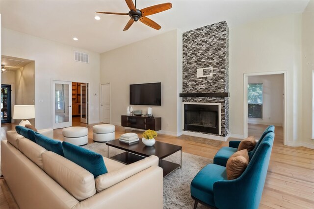 dining space with a high ceiling, light hardwood / wood-style flooring, a large fireplace, ceiling fan, and french doors