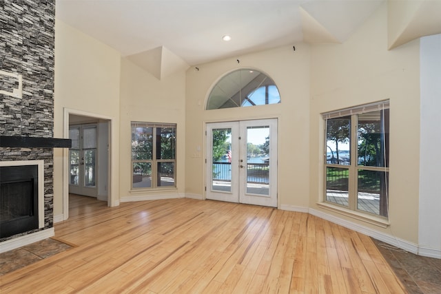 unfurnished living room featuring french doors, a stone fireplace, light hardwood / wood-style flooring, and high vaulted ceiling