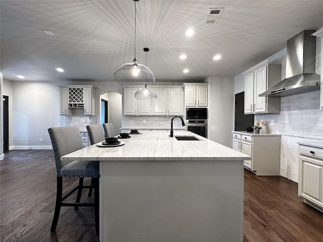 kitchen with a large island with sink, oven, dark hardwood / wood-style flooring, wall chimney exhaust hood, and white cabinets