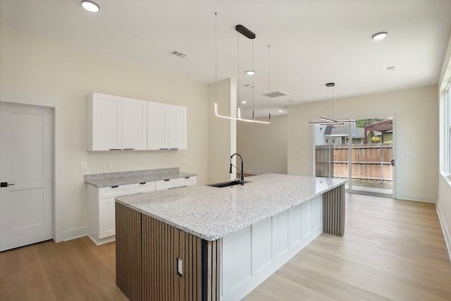 kitchen with white cabinets, sink, a kitchen island with sink, decorative light fixtures, and light stone countertops