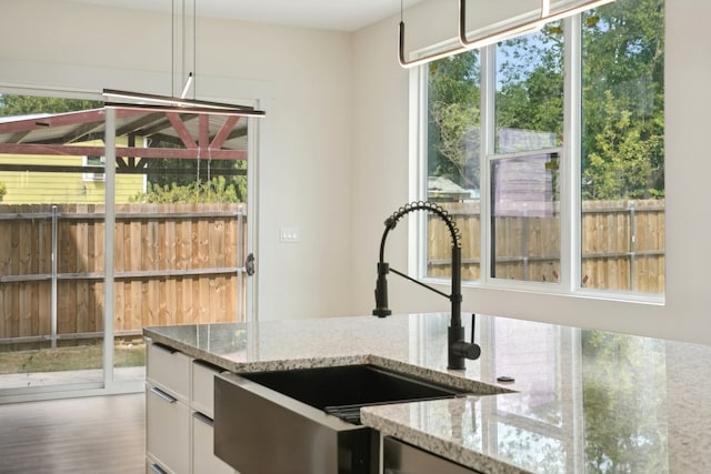 kitchen with hardwood / wood-style flooring, light stone countertops, pendant lighting, and a wealth of natural light