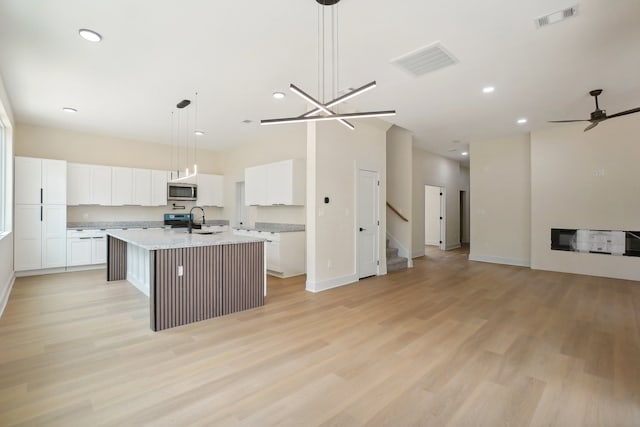 kitchen featuring pendant lighting, an island with sink, light hardwood / wood-style flooring, stainless steel appliances, and ceiling fan with notable chandelier