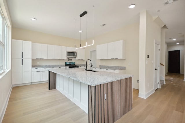 kitchen featuring light stone counters, white cabinets, an island with sink, sink, and light hardwood / wood-style flooring