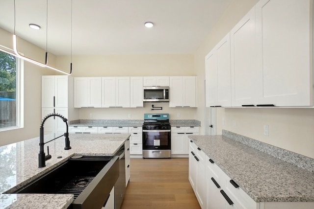 kitchen with stainless steel appliances, white cabinetry, and hanging light fixtures