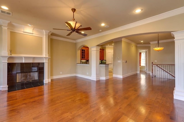 unfurnished living room featuring ornamental molding, a tile fireplace, dark hardwood / wood-style flooring, ceiling fan, and ornate columns