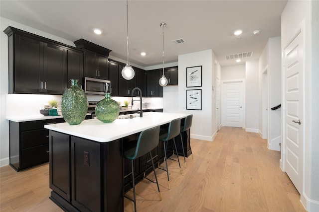 kitchen featuring decorative light fixtures, decorative backsplash, a kitchen breakfast bar, light wood-type flooring, and a center island with sink