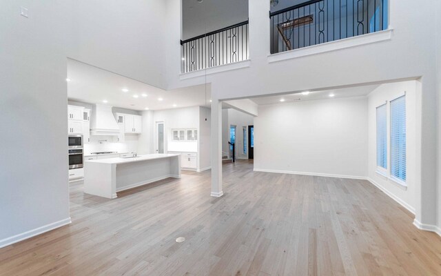 unfurnished living room featuring light wood-type flooring, a towering ceiling, and sink