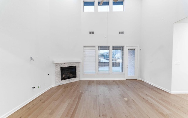 unfurnished living room featuring light wood-type flooring, a wealth of natural light, ceiling fan, a high ceiling, and a stone fireplace