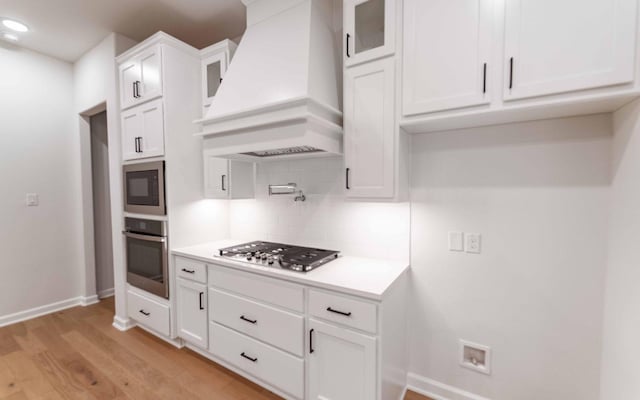 kitchen featuring stainless steel appliances, decorative backsplash, white cabinets, custom range hood, and light wood-type flooring