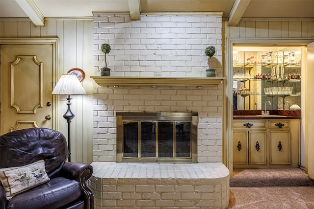 carpeted living room with a fireplace, crown molding, beam ceiling, and sink