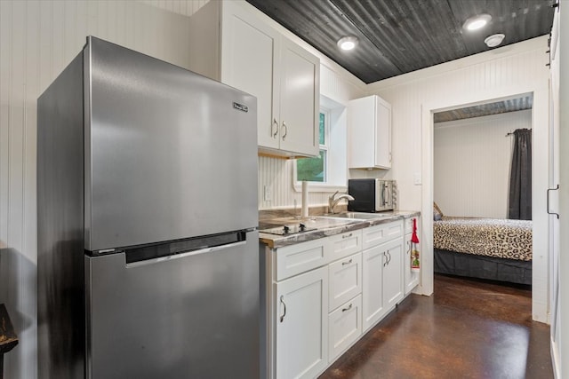 kitchen with stainless steel refrigerator, wood walls, sink, light stone countertops, and white cabinets