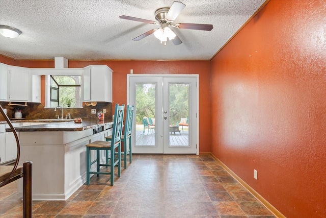 kitchen with sink, ceiling fan, a breakfast bar, french doors, and white cabinets