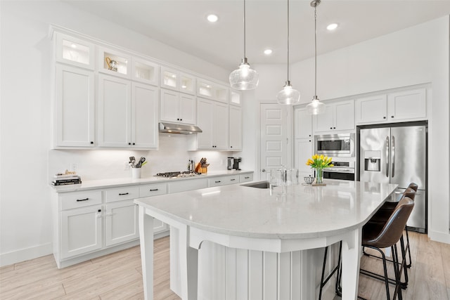 kitchen featuring a kitchen island with sink, decorative light fixtures, stainless steel appliances, a breakfast bar, and white cabinets