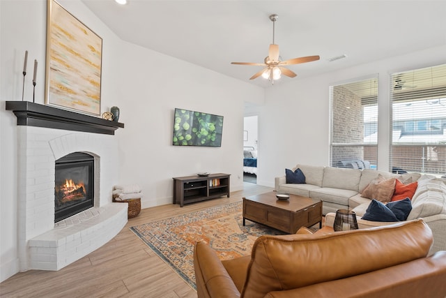 living room with light wood-type flooring, ceiling fan, and a brick fireplace