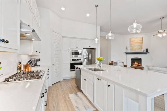 kitchen featuring white cabinets, a brick fireplace, stainless steel appliances, ceiling fan, and a kitchen island with sink