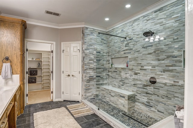 bathroom with a tile shower, vanity, and ornamental molding