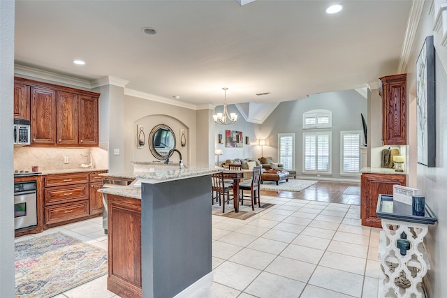 kitchen with appliances with stainless steel finishes, an island with sink, a chandelier, light tile patterned floors, and ornamental molding