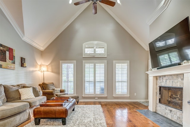 living room with ceiling fan, crown molding, wood-type flooring, high vaulted ceiling, and a fireplace