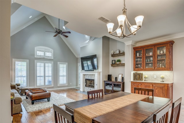 dining area featuring high vaulted ceiling, a high end fireplace, ceiling fan with notable chandelier, crown molding, and light wood-type flooring