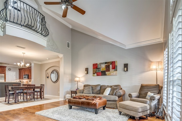 living room with a towering ceiling, ceiling fan with notable chandelier, light hardwood / wood-style floors, and ornamental molding