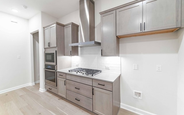 kitchen with decorative backsplash, wall chimney exhaust hood, light hardwood / wood-style floors, stainless steel appliances, and gray cabinets