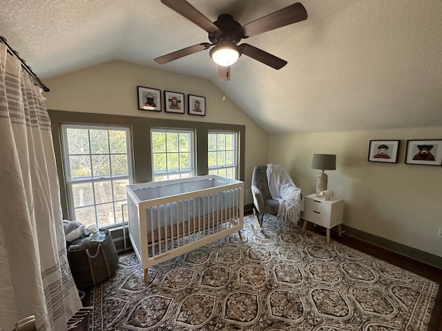 bedroom featuring a textured ceiling, lofted ceiling, ceiling fan, and a nursery area