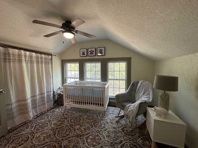 bedroom with lofted ceiling, a textured ceiling, a crib, and ceiling fan