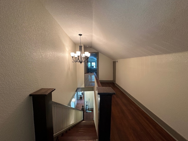 stairs with wood-type flooring, an inviting chandelier, vaulted ceiling, and a textured ceiling