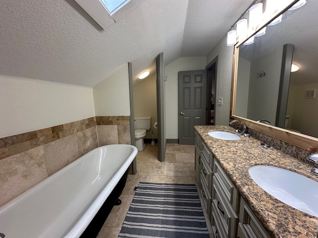 bathroom featuring vanity, a skylight, a textured ceiling, a bathing tub, and toilet