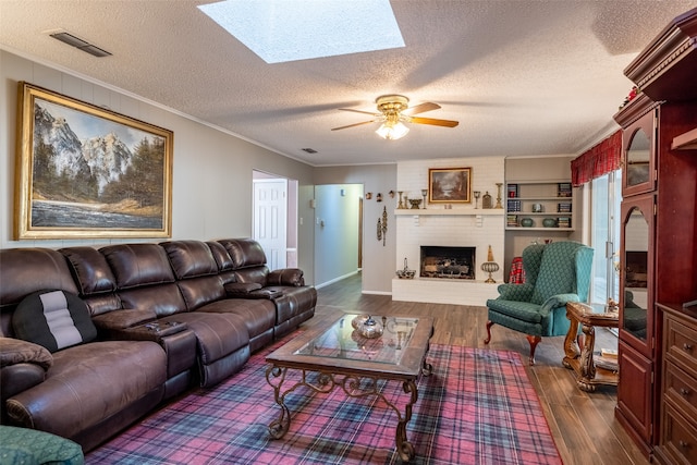 living room featuring a skylight, a fireplace, dark wood-type flooring, ceiling fan, and a textured ceiling